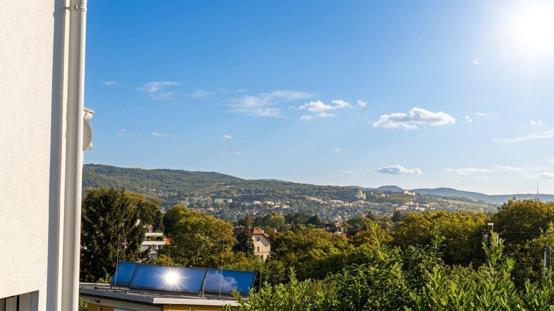 Weitläufiger Blick über die grüne Landschaft und Dächer der Umgebung an einem sonnigen Tag.