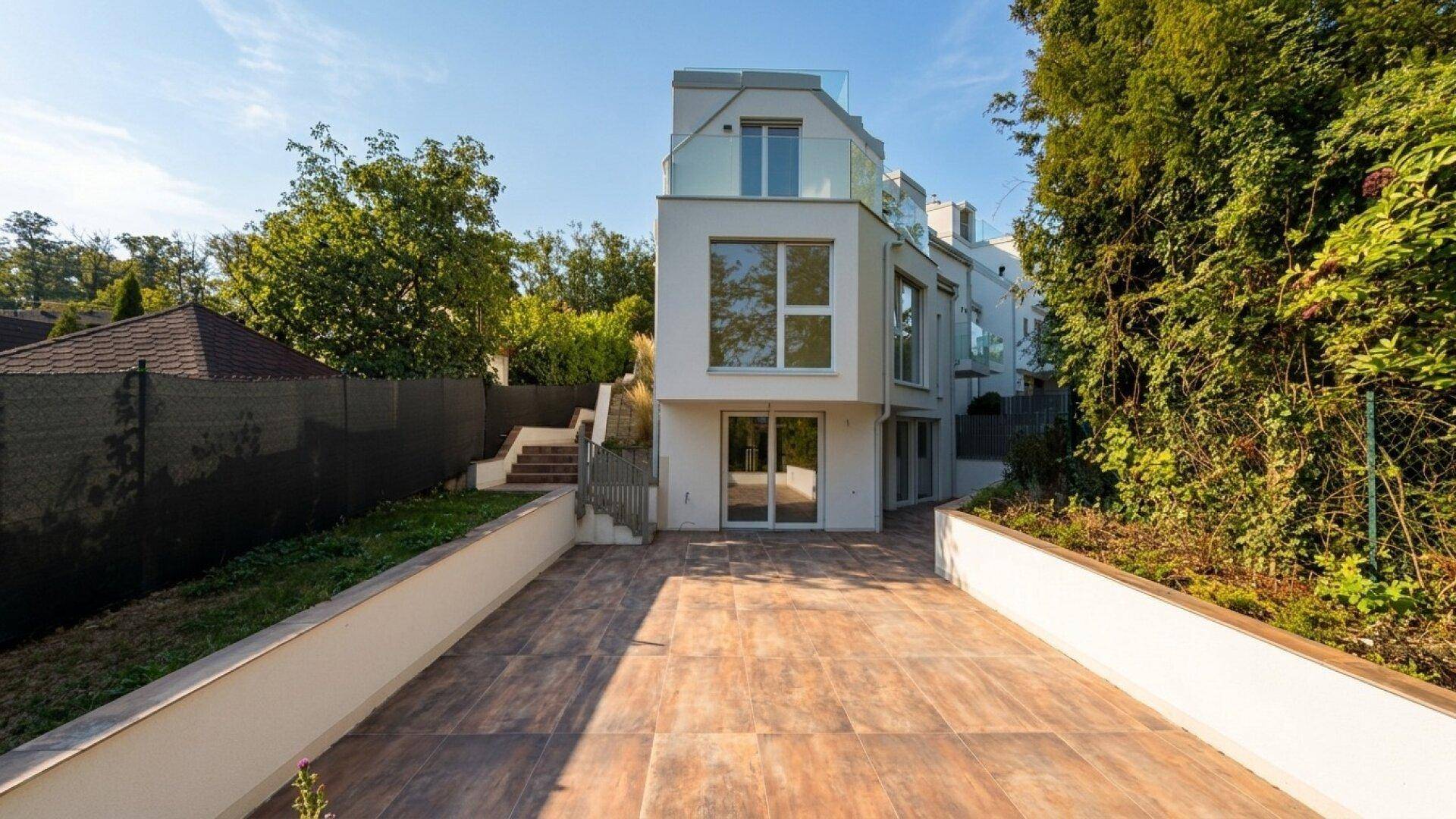 Hinterer Bereich des Hauses mit großer gepflasterter Terrasse und Treppenaufgang zum Garten.