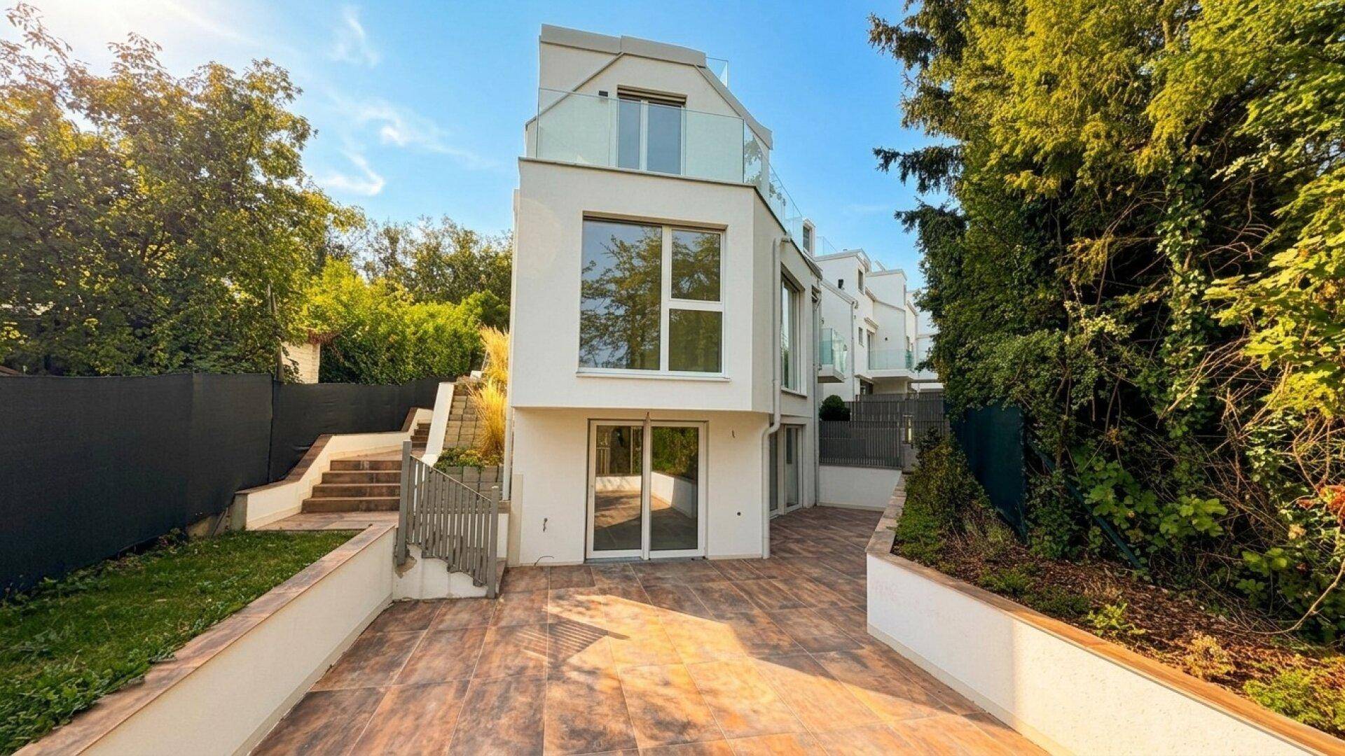 Moderne weiße Stadtvilla mit großen Fenstern und Glasbalkonen, umgeben von üppigem Grün.
