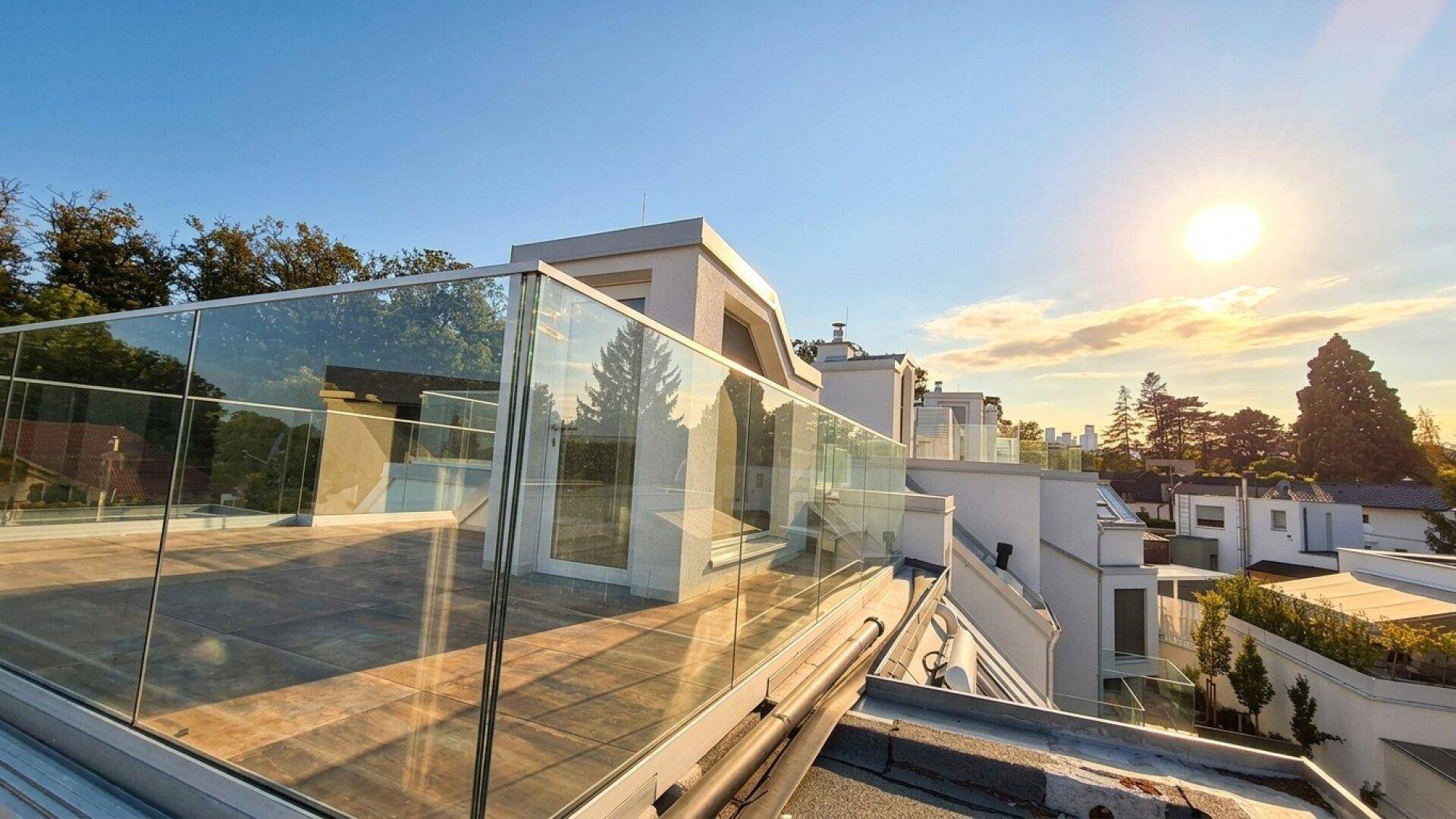 Geräumige Dachterrasse mit Glasgeländer und weitem Blick in die Ferne bei Sonnenuntergang.
