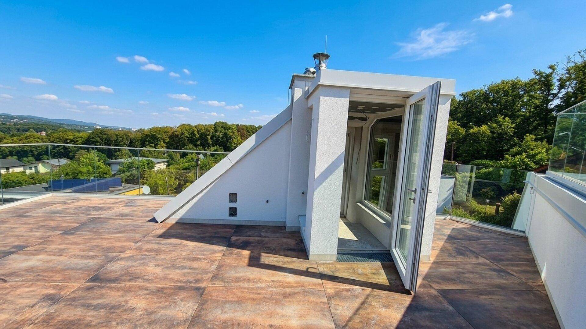 Geräumige Dachterrasse mit Glasgeländer und weitem Blick über die grüne Landschaft und Häuser.
