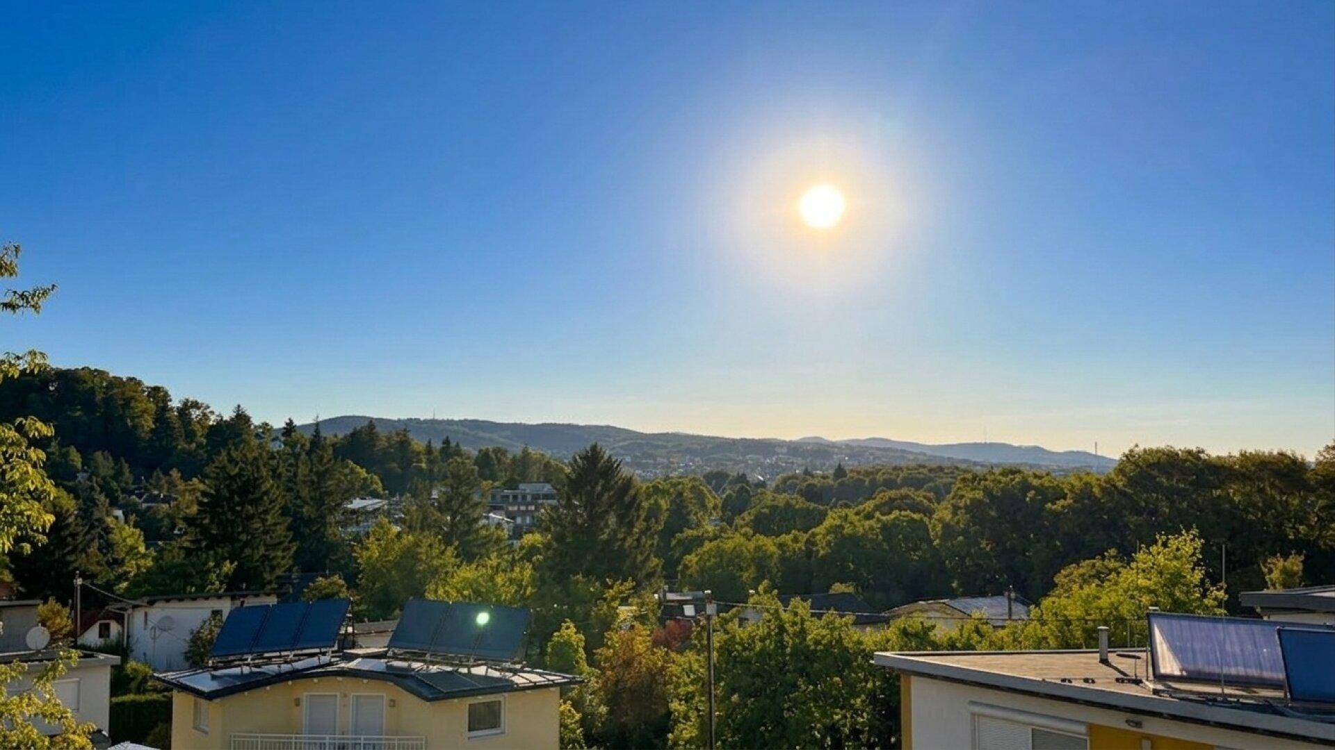 Weitläufiger Blick über grüne Hügel und Dächer unter strahlend blauem Himmel.