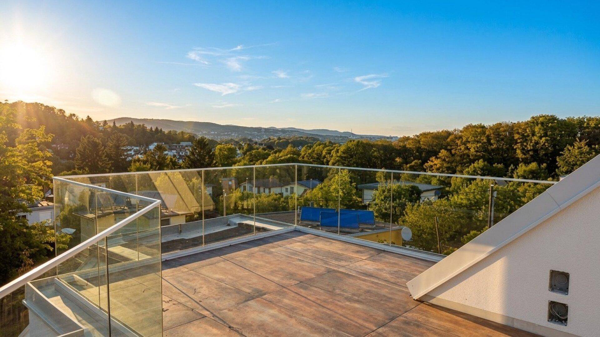 Weitläufige Dachterrasse mit Glasgeländer und beeindruckendem Ausblick auf die umliegende Natur und Häuser.