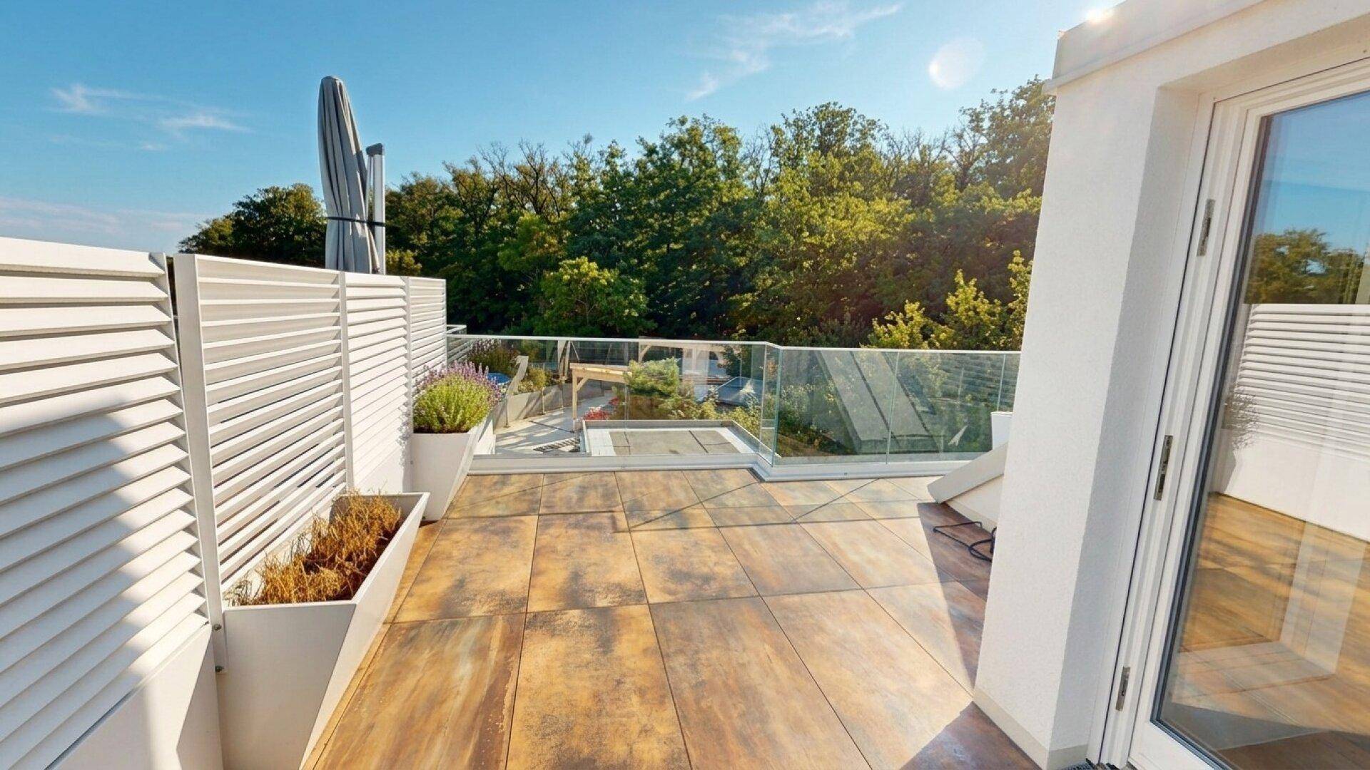 Helle Terrasse mit modernen Fliesen, Sichtschutz und Blick auf die umliegende Natur.