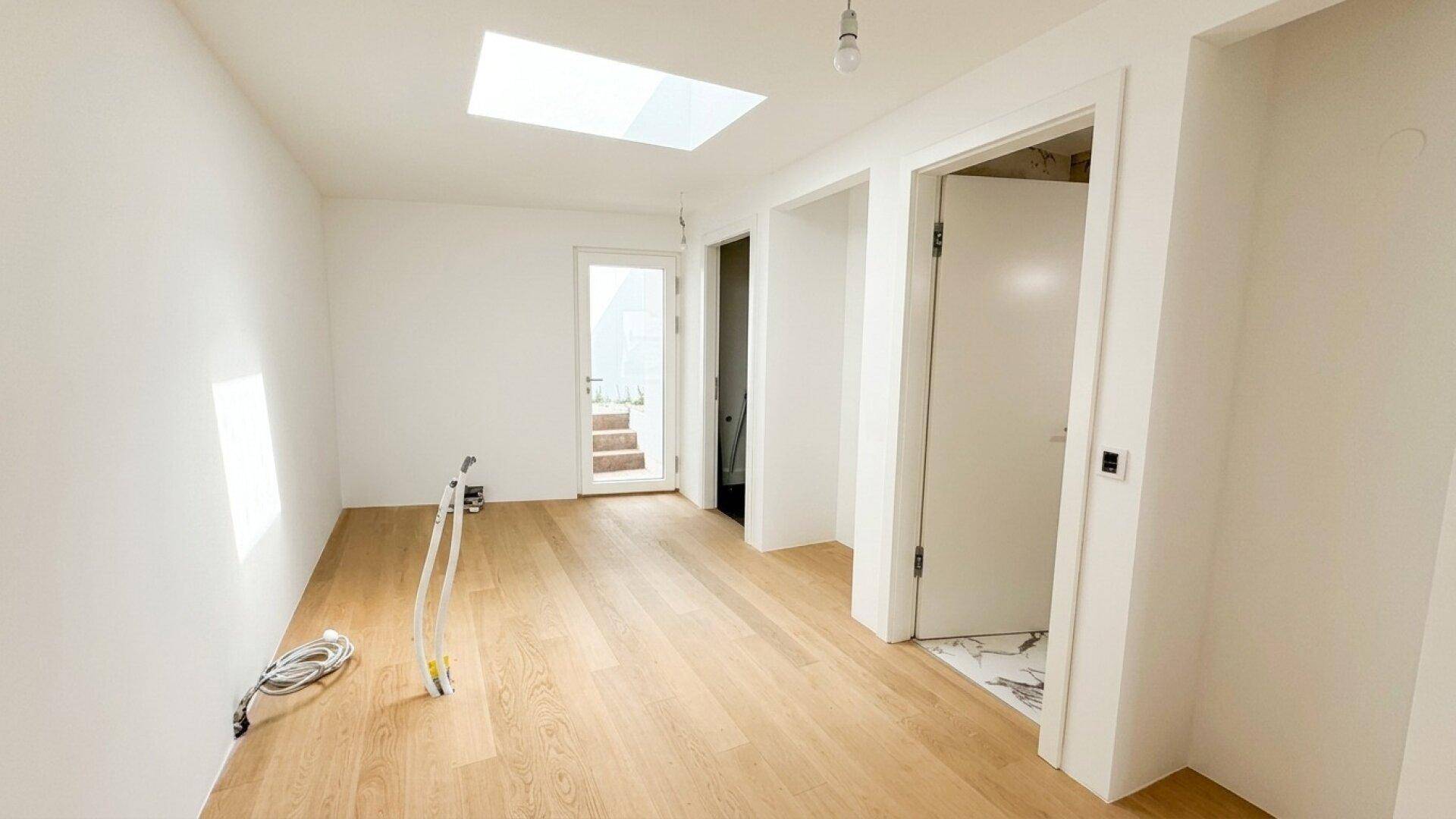 Heller Flur mit Holzfußboden, weißen Wänden und einem großen Oberlicht für viel Tageslicht.