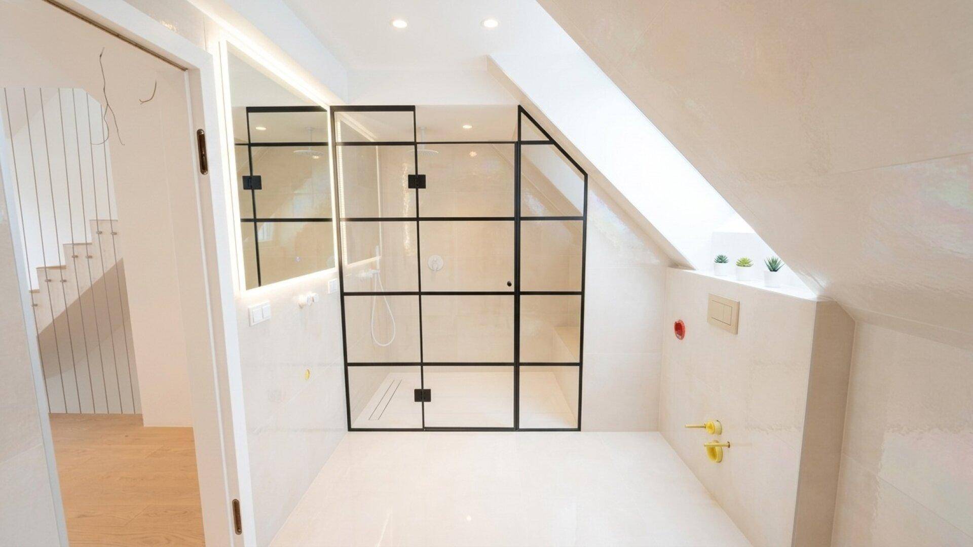 Unfertiges Badezimmer mit moderner Duschkabine und Spiegel unter der Dachschräge.