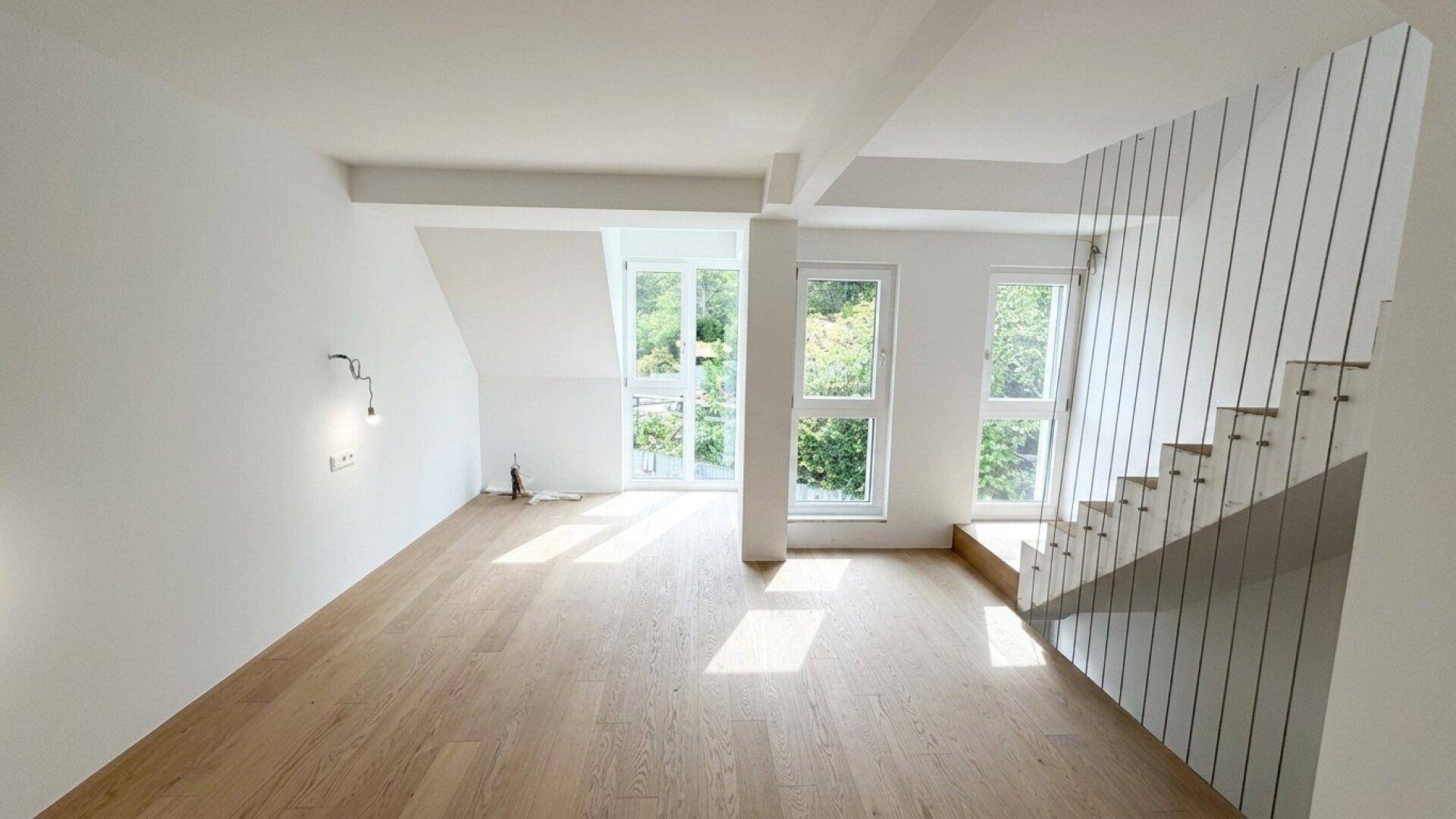Heller Wohnbereich im Obergeschoss mit Holzfußboden, großen Fenstern und moderner Treppe.