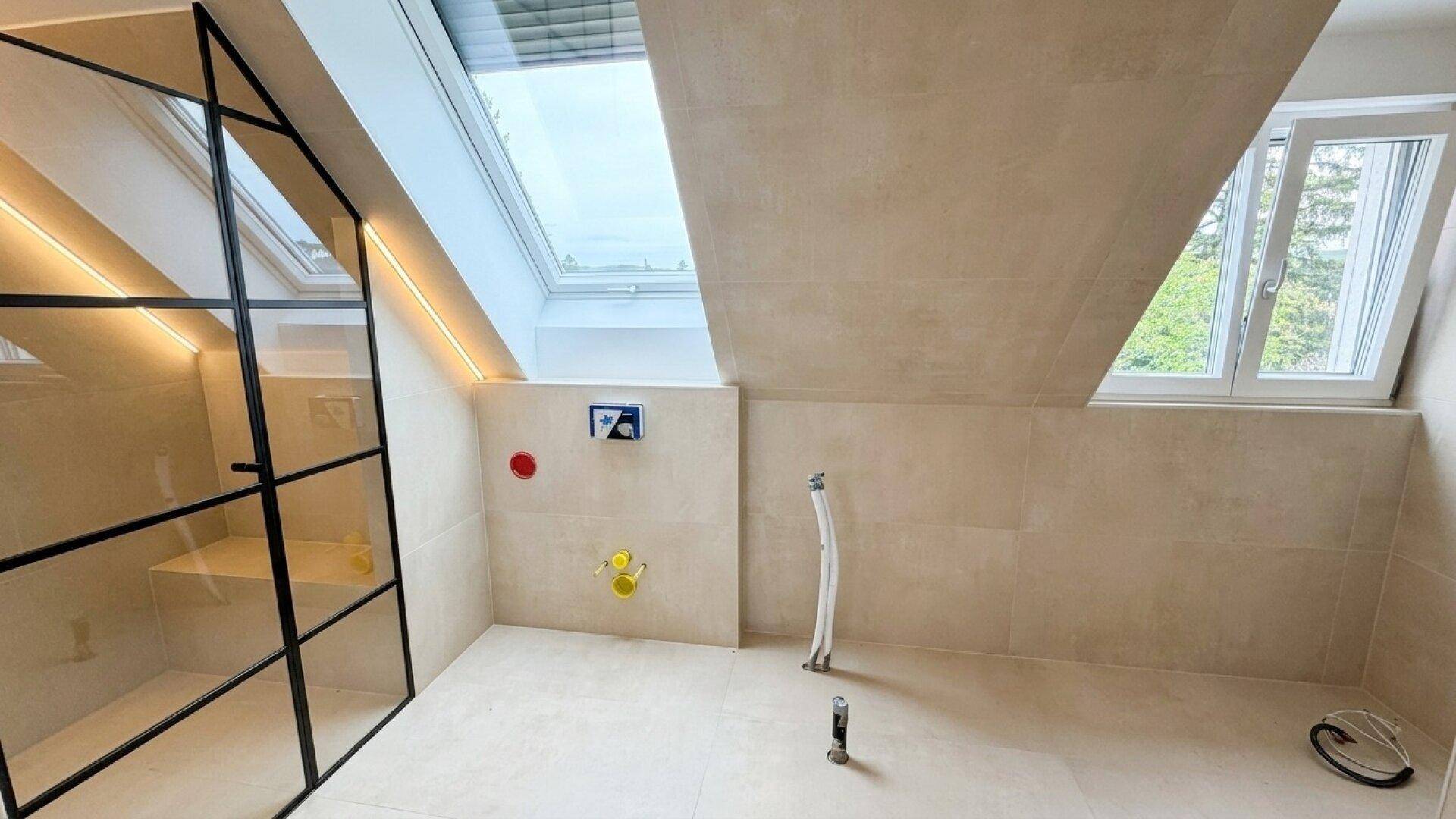 Unfertiges Badezimmer mit Installationen für Badewanne und Dusche unter Dachschräge.