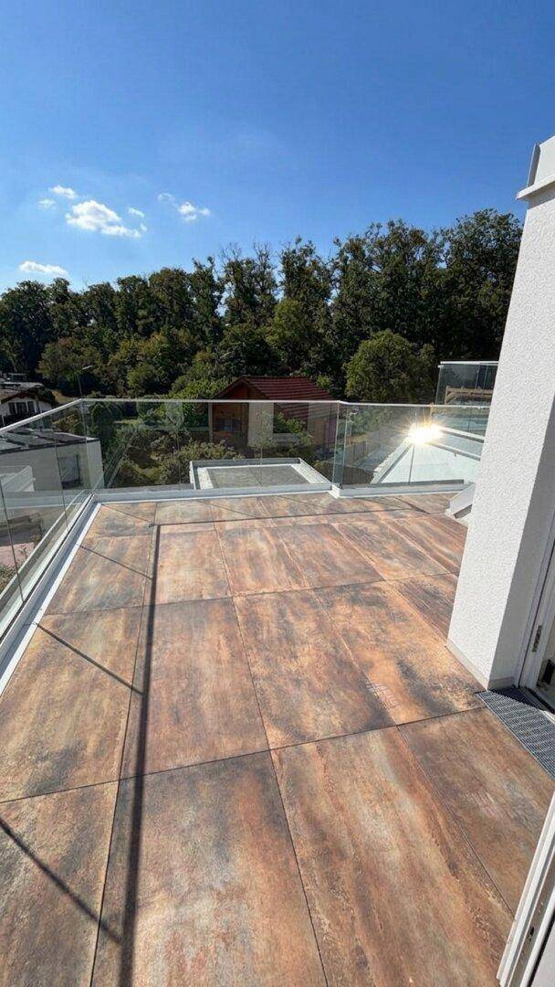 Geräumige Terrasse mit modernen Fliesen, Glasgeländer und weitem Blick ins Grüne.
