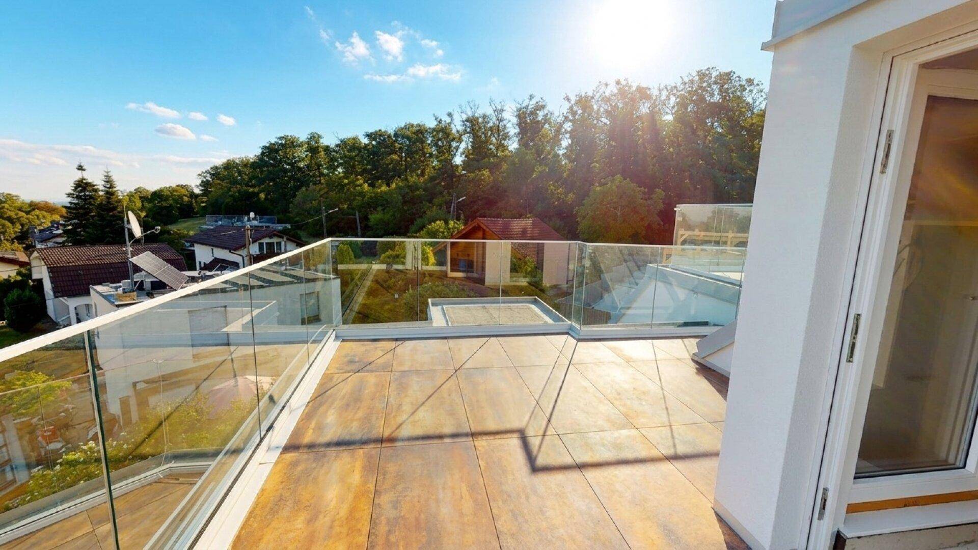 Sonniger Terrassenbereich mit modernen Fliesen, Glasgeländer und Blick auf die Natur.