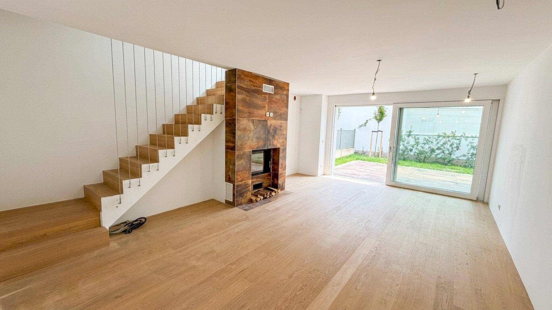 Heller Wohnbereich mit Kamin, Holzfußboden und Zugang zur Terrasse durch große Schiebetüren.