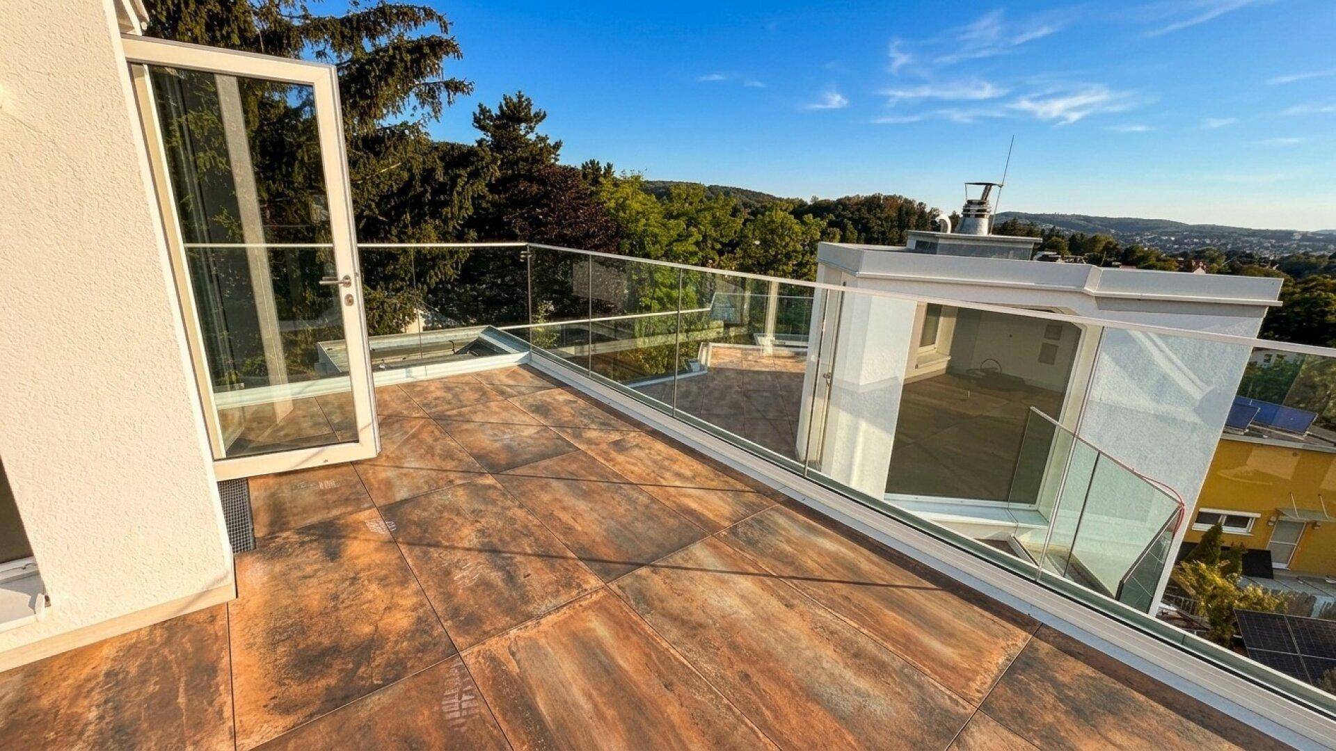 Geräumige Dachterrasse mit modernen Glasgeländern und weitem Blick ins Grüne unter blauem Himmel.