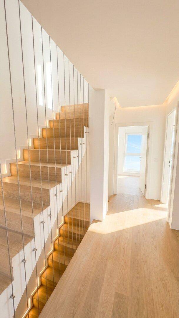 Heller Flur mit moderner Holztreppe, indirekter Beleuchtung und viel Tageslicht.