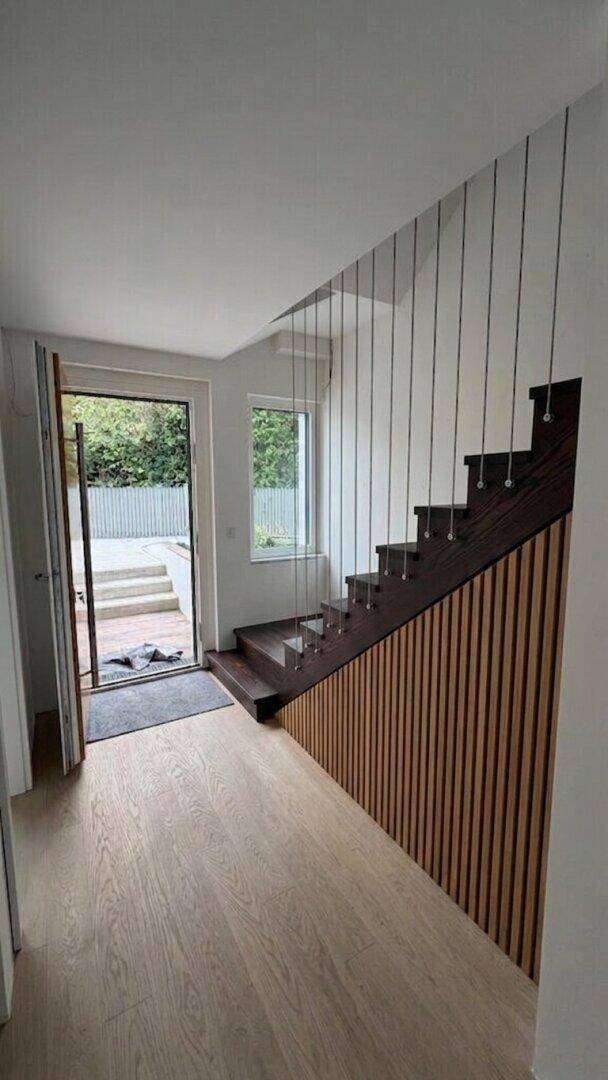 Moderner Eingangsbereich mit Holztreppe und Zugang zu einem Außenbereich.