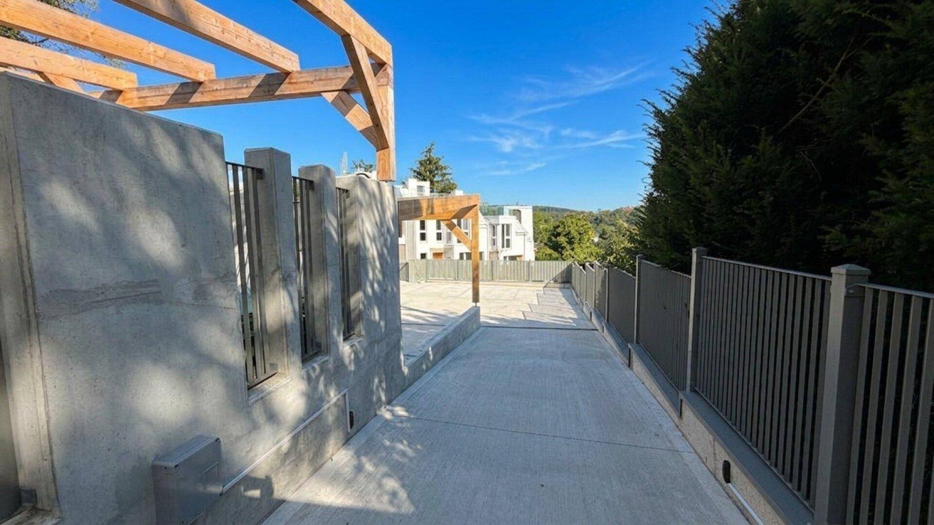 Zufahrtsweg aus Beton zu den Parkplätzen mit Blick auf die modernen Gebäude.