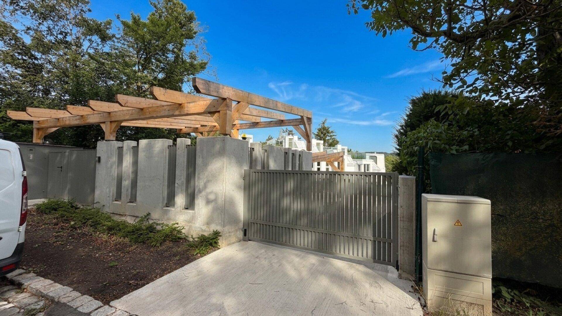 Eingangsbereich mit modernem Tor und einer Holzpergola, umgeben von Grünflächen.
