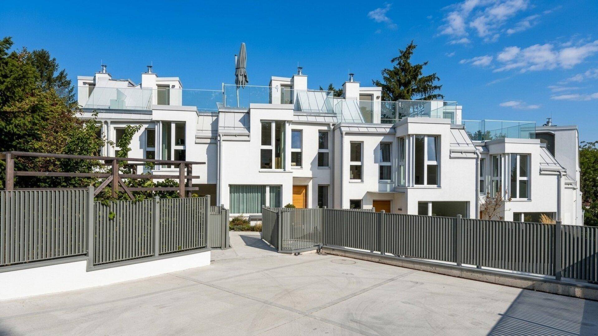 Moderne Reihenhäuser mit weißer Fassade und großen Fenstern unter blauem Himmel.