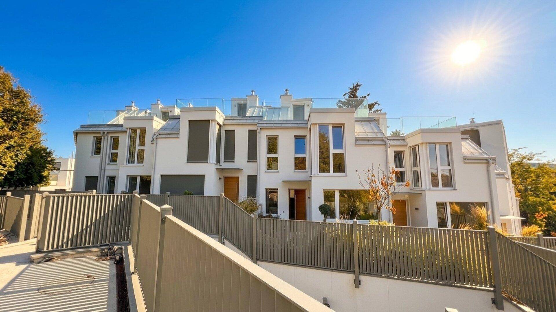 Sonnenbeschienene moderne Reihenhäuser mit großen Fenstern und Terrassen.
