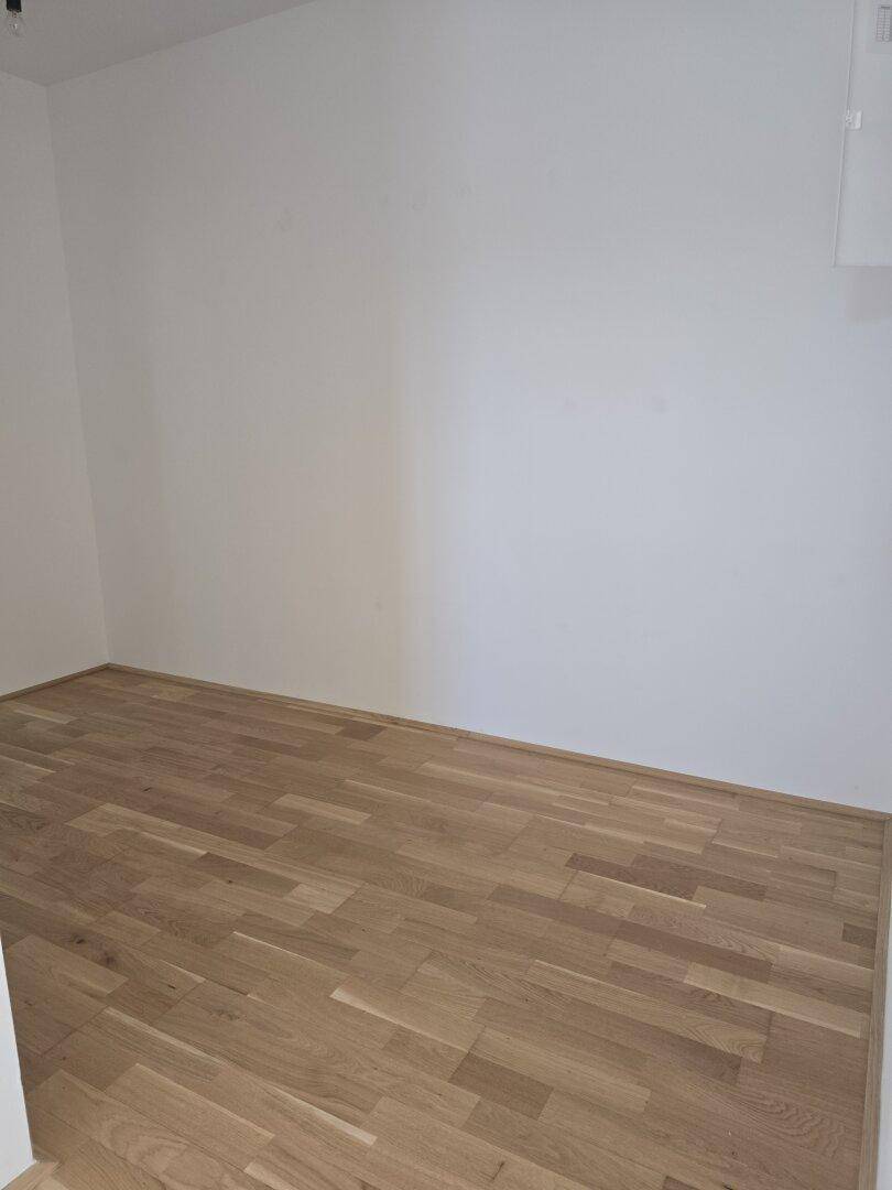Leerer Raum mit hellem Holzfußboden und weißen Wänden, bereit zur individuellen Einrichtung.