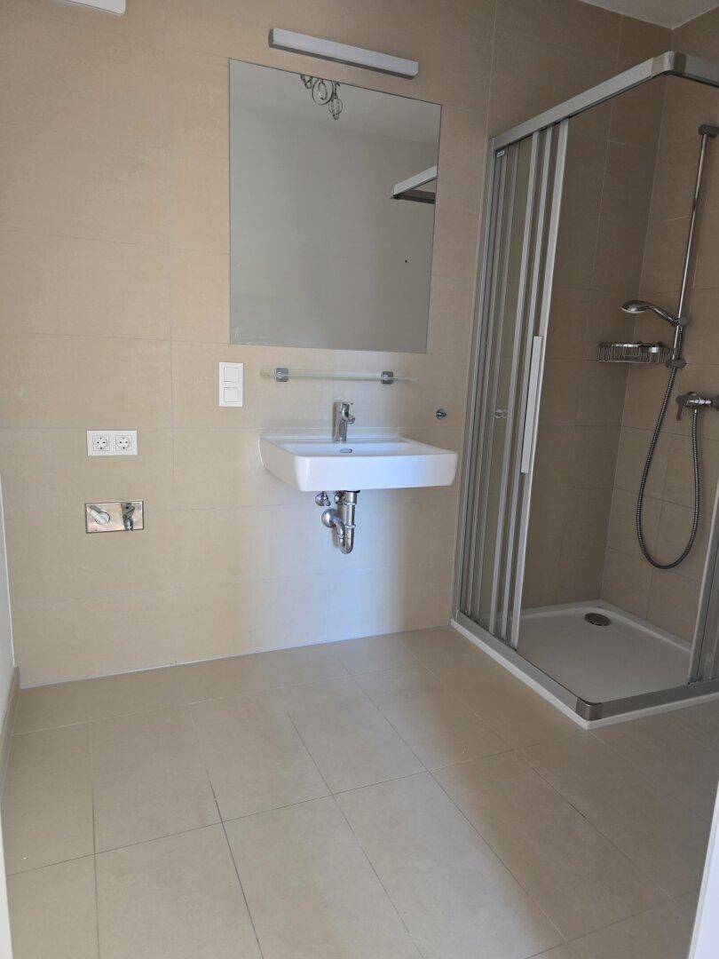 Helles Badezimmer mit Duschkabine und Waschbecken, neutral gefliest und pflegeleicht.