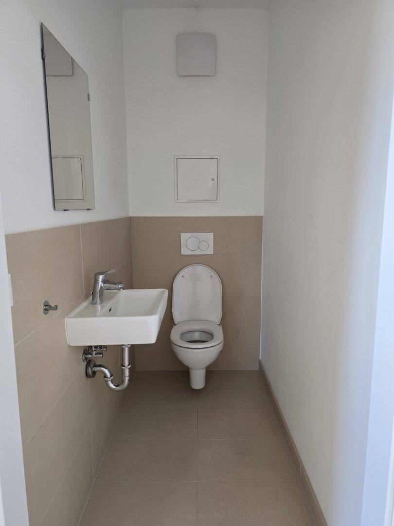 Modernes Gäste-WC mit Wand-WC und kleinem Waschbecken, hell und funktional gefliest.