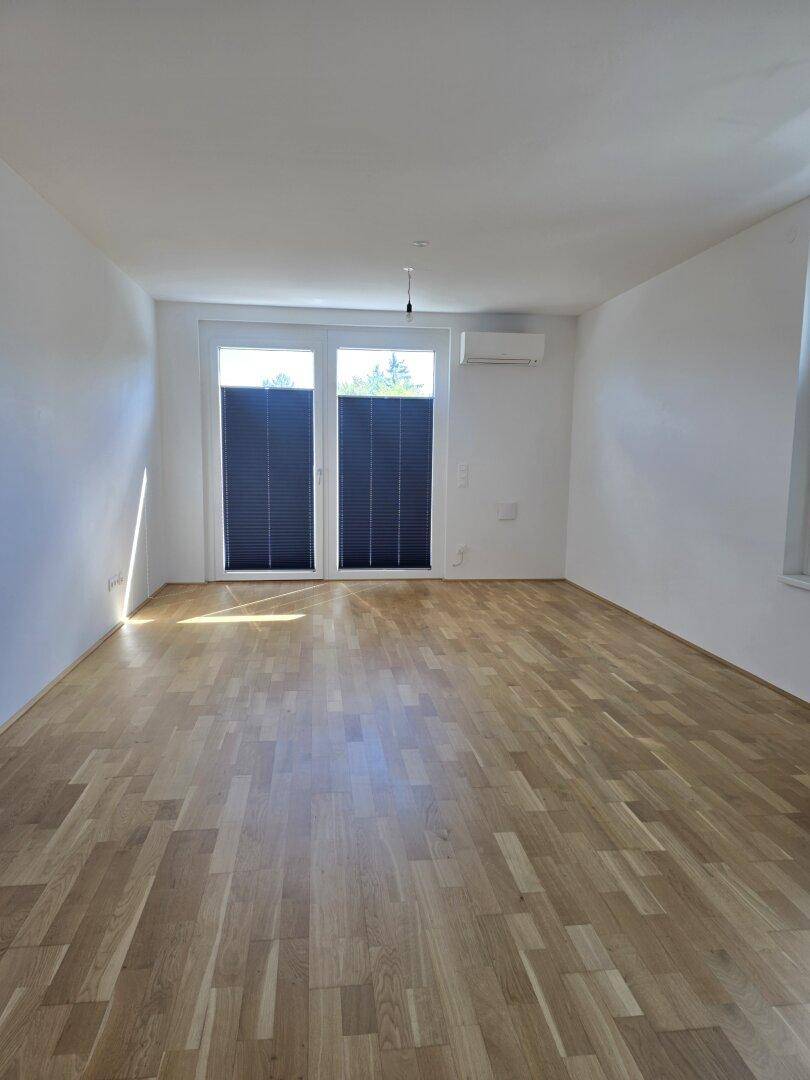 Heller Raum mit Holzfußboden, Klimaanlage und Zugang zu einem sonnigen Außenbereich.