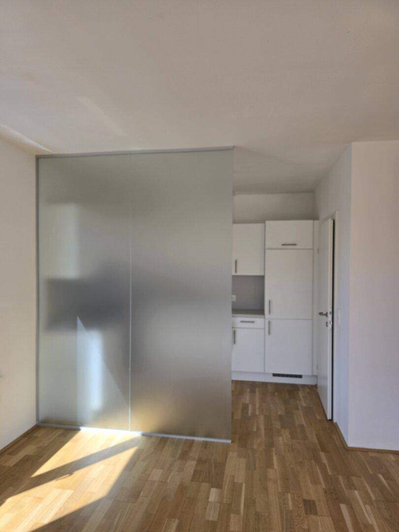 Helle Küche mit weißen Schränken, teilweise abgetrennt durch eine moderne Glaswand.