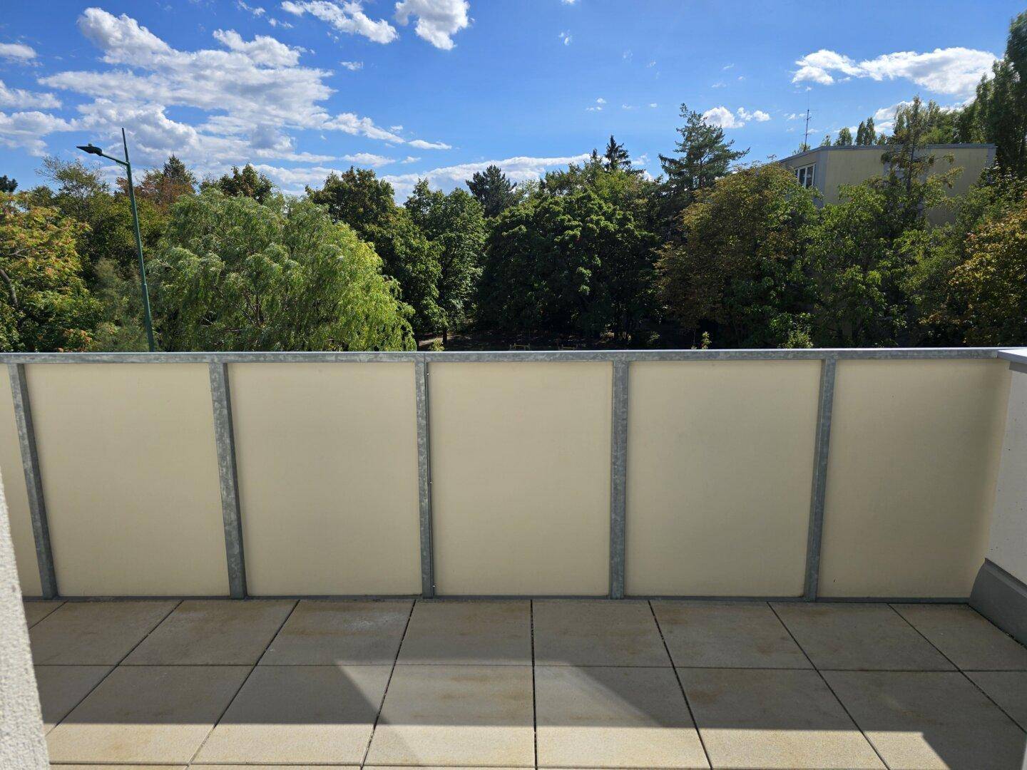 Geräumiger Balkon mit Fliesenboden und weitem Blick ins Grüne unter blauem Himmel.