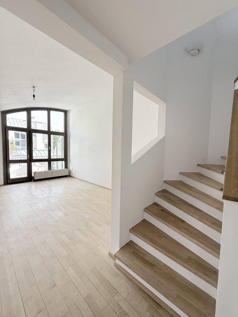 Geräumiger Wohnbereich mit hellem Holzparkett und einem großen, bogenförmigen Fenster, das viel Licht spendet.