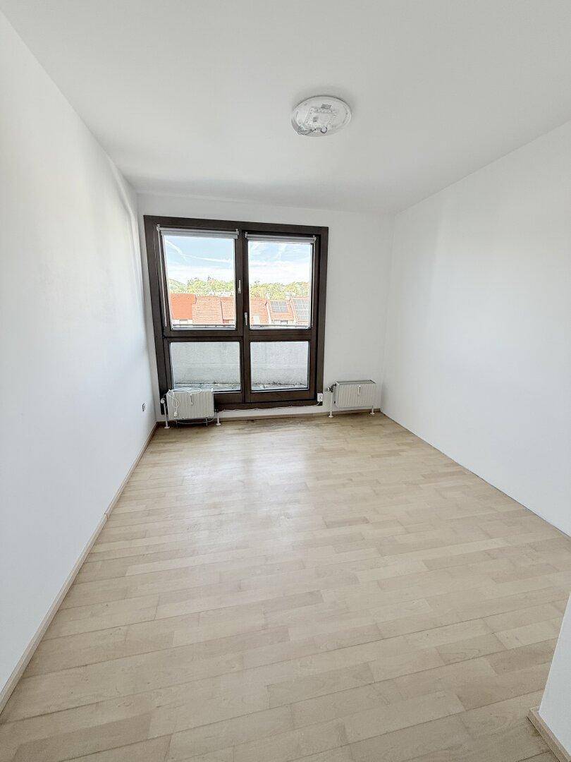 Geräumiges Zimmer mit hellem Holzparkett, weißen Wänden und einem großen Fenster für viel Helligkeit.