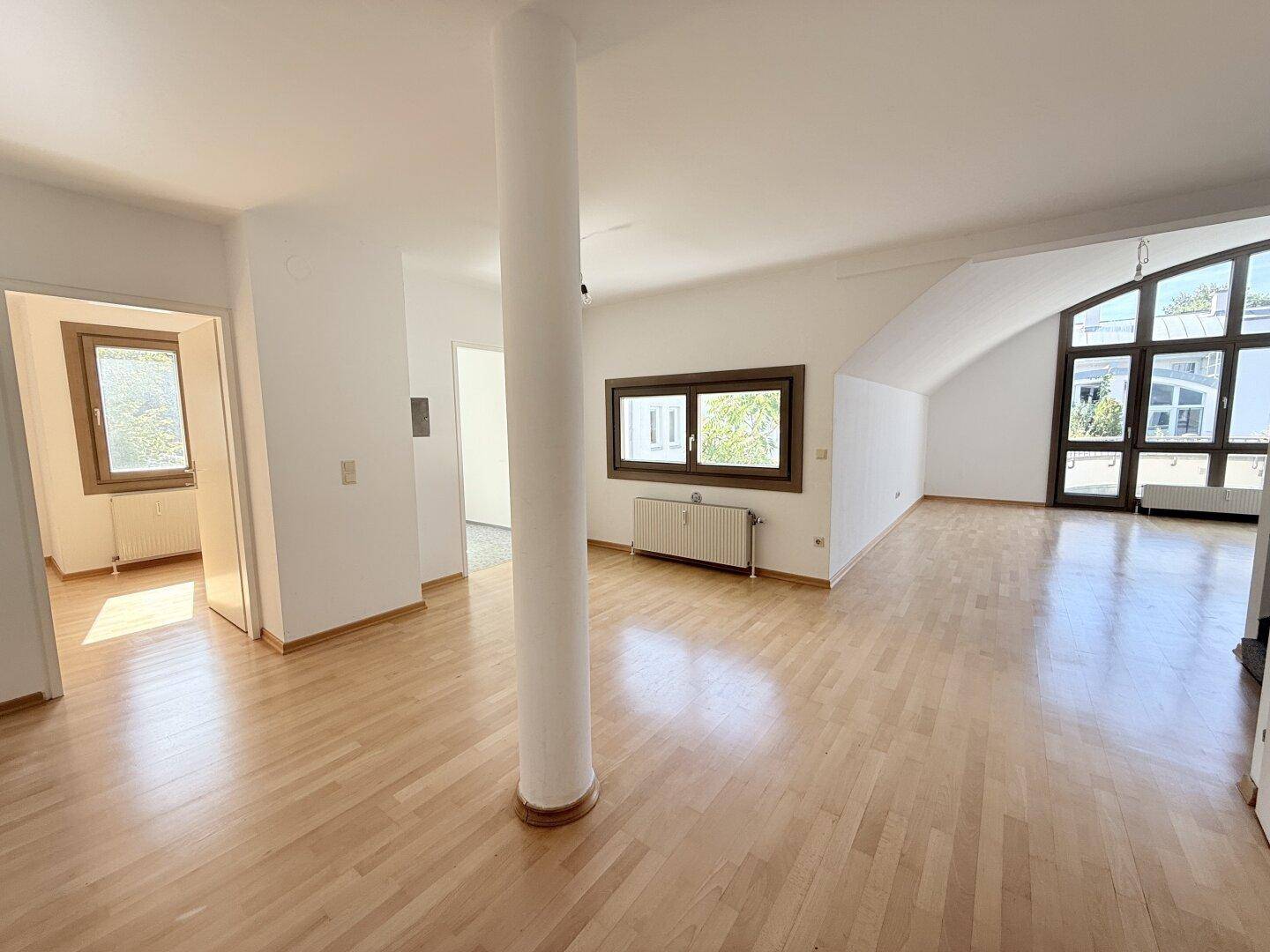 Helles, leeres Wohnzimmer mit Holzparkettboden, Säule und großen Fenstern im Dachgeschoss.