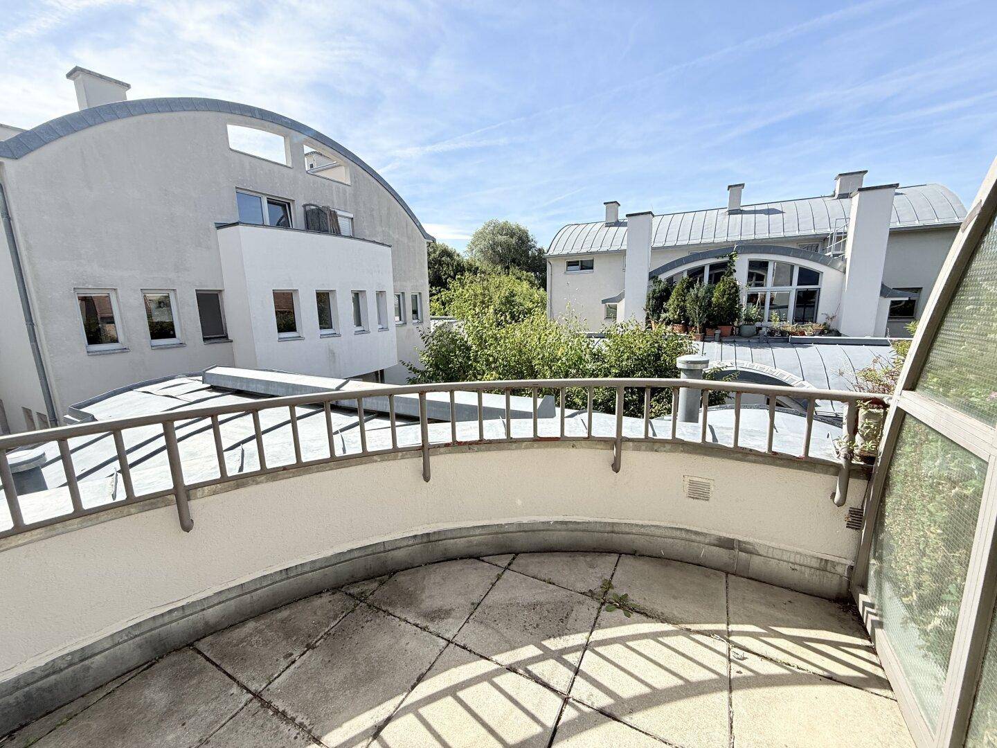 Weitläufige Dachterrasse mit Fliesen und Blick auf die moderne Architektur der Nachbargebäude.