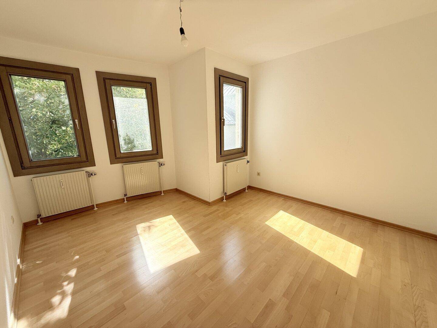 Helles Schlafzimmer mit Parkettboden, drei Fenstern und viel natürlichem Lichteinfall.