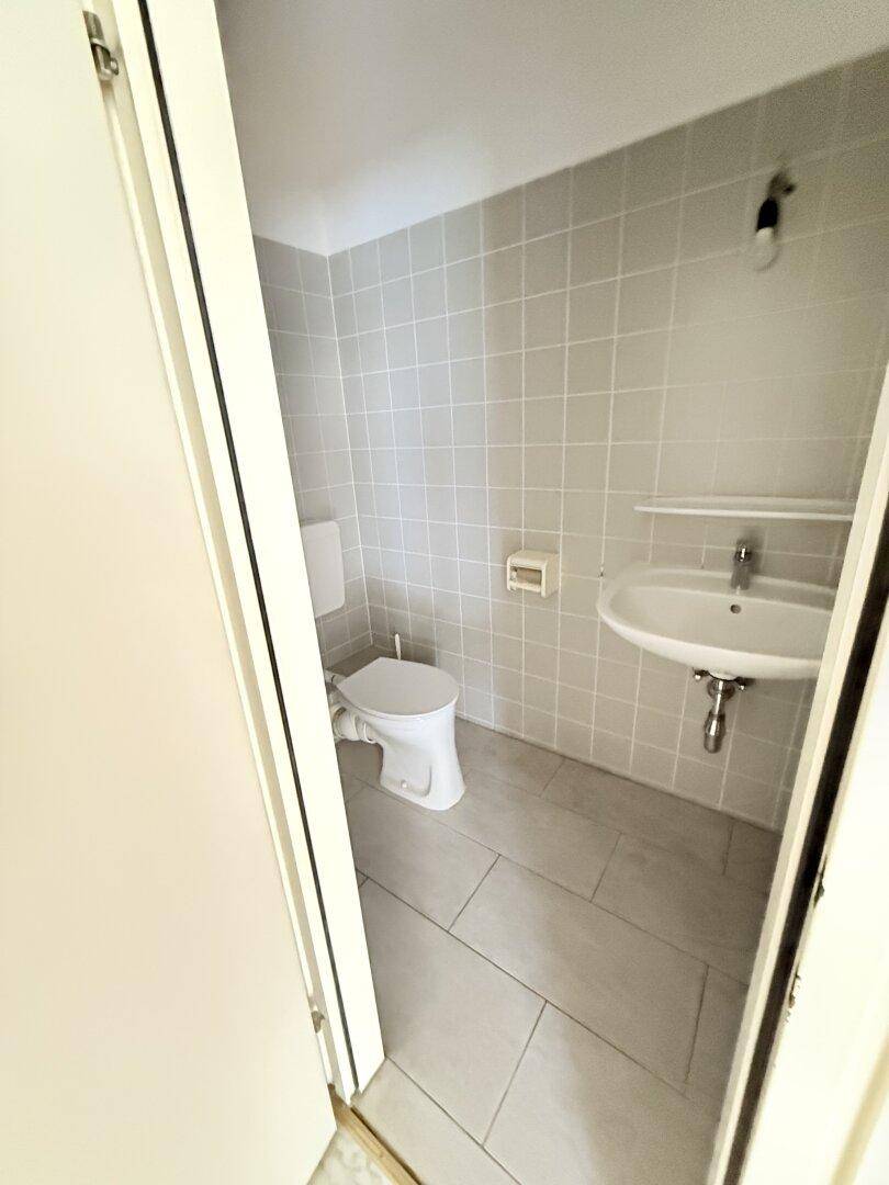 Gäste-WC mit hellgrauen Fliesen, Toilette und Waschbecken, gut erhalten.