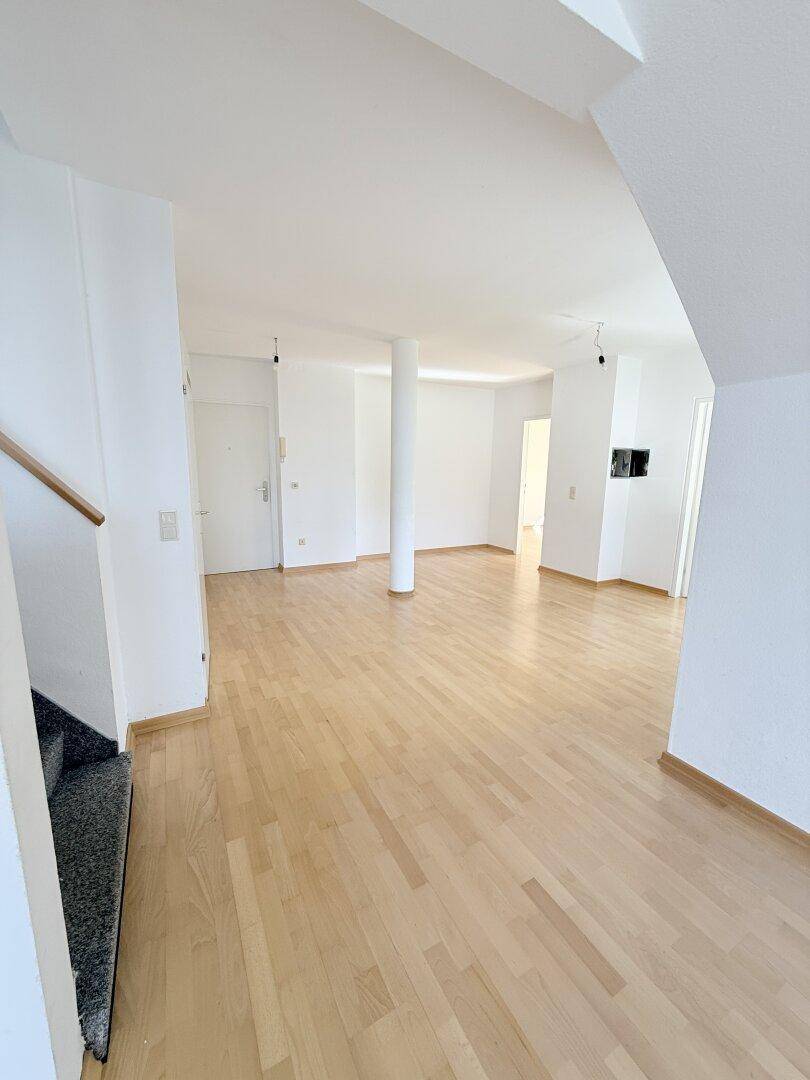 Geräumiger Wohnbereich mit hellem Parkettboden, weiß gestrichenen Wänden und Säulen.