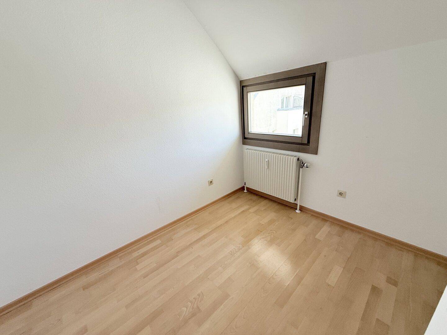 Kleines Schlafzimmer mit Parkettboden, Heizung und einem Fenster mit Blick nach draußen.