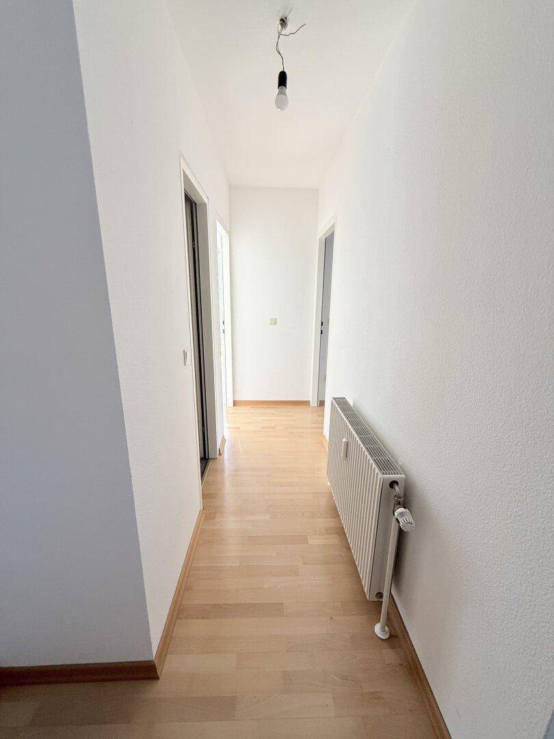 Heller Flur mit Parkettboden und Heizkörper, verbindet verschiedene Zimmer.