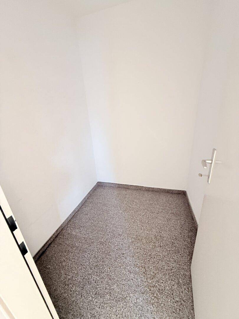Kleiner Abstellraum mit grauem Terrazzoboden und weißen Wänden.