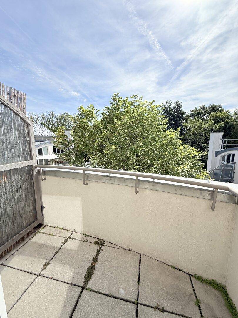 Kleiner Balkon mit Fliesenboden und Blick auf grüne Bäume und den Himmel.