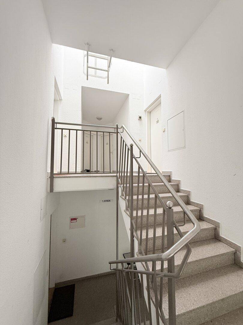 Treppenhaus mit Teppichboden und Metallgeländer, führt zu den oberen Etagen.