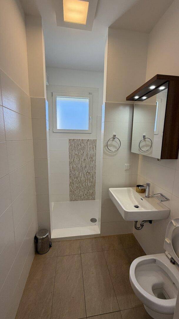 Modernes Badezimmer mit weißen Fliesen, ebenerdiger Dusche, Einzelwaschbecken und Fenster.