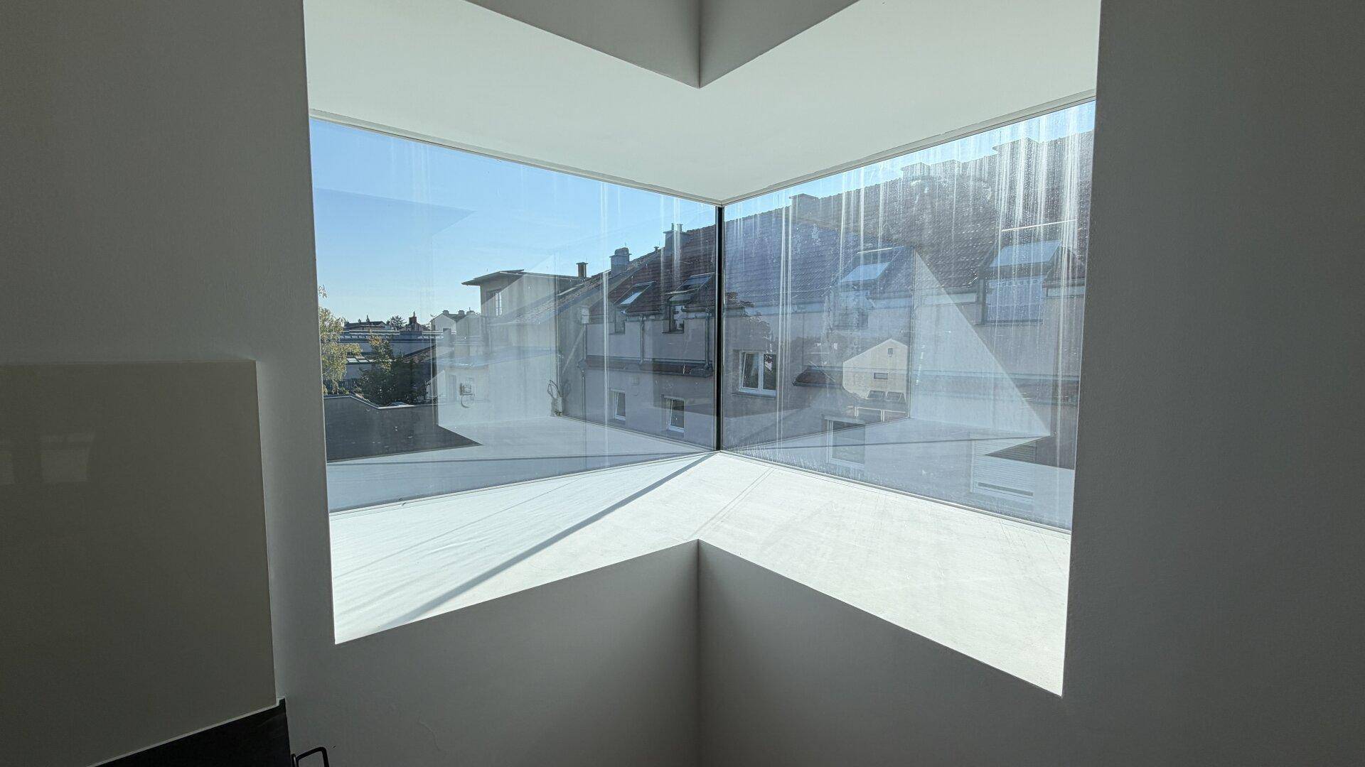 Innenansicht durch ein großes, modernes Eckfenster mit Blick auf die Dächer der Stadt.