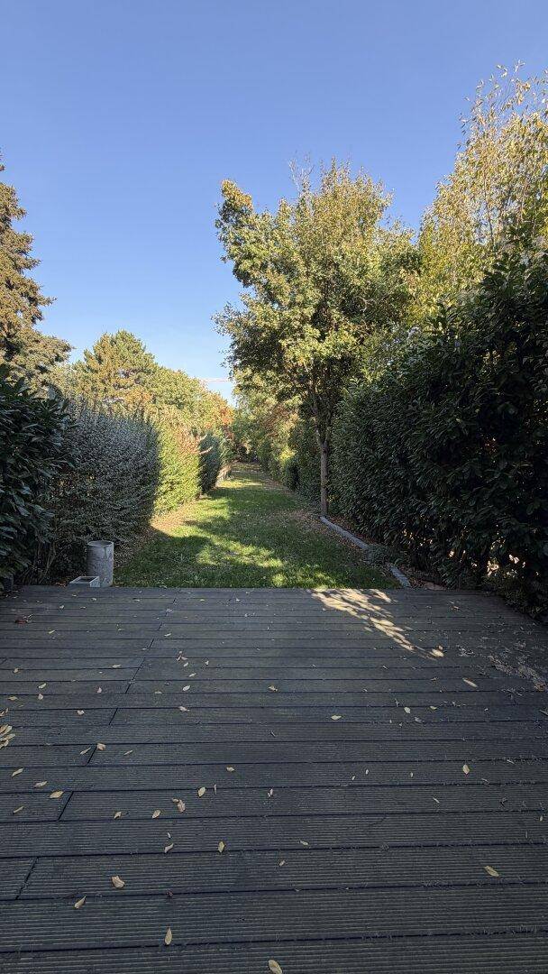 Weitläufiger Gartenbereich mit Holzterrasse und langem Rasenweg, umgeben von Hecken.