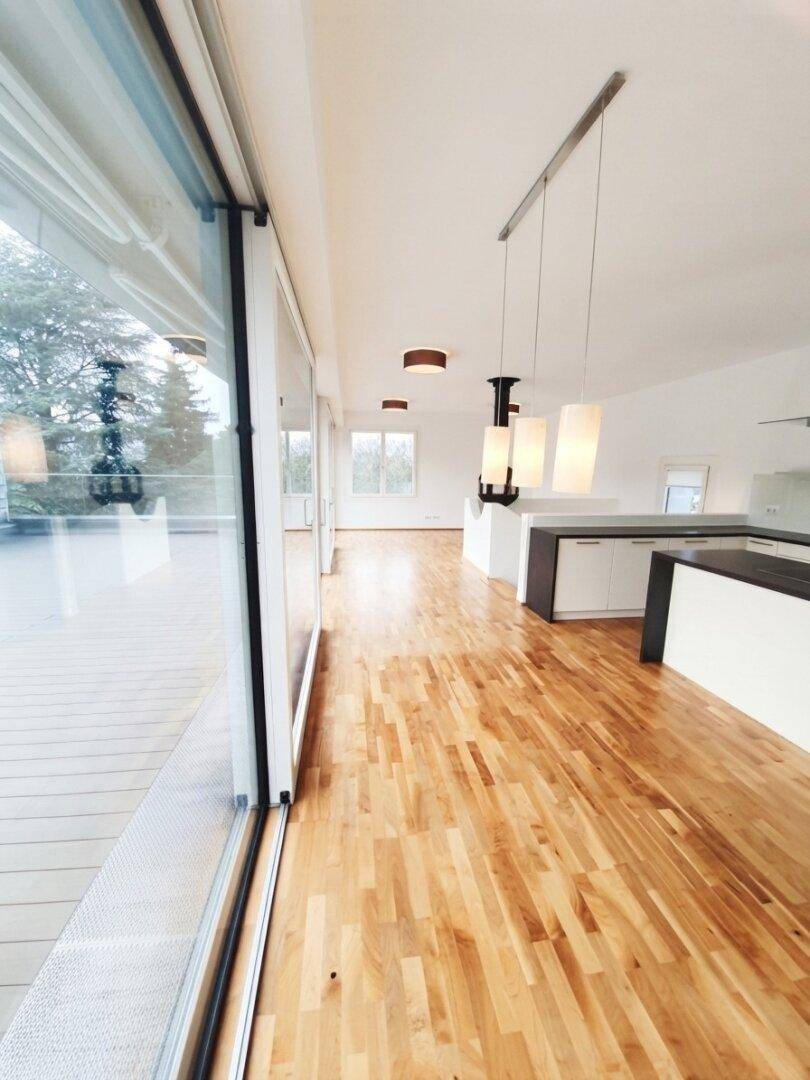 Heller offener Wohnbereich mit Holzboden und Zugang zur Terrasse, moderne Pendelleuchten.
