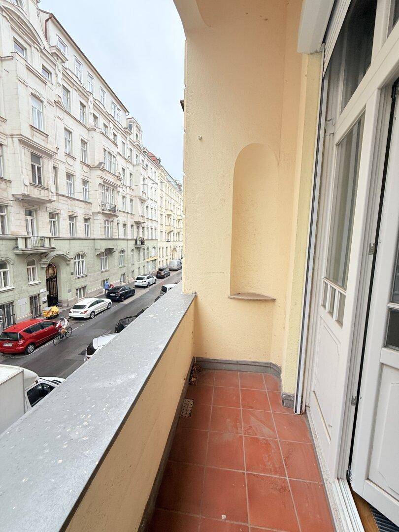 Balkon mit Terrakottafliesen und Blick auf die Straße mit parkenden Autos.
