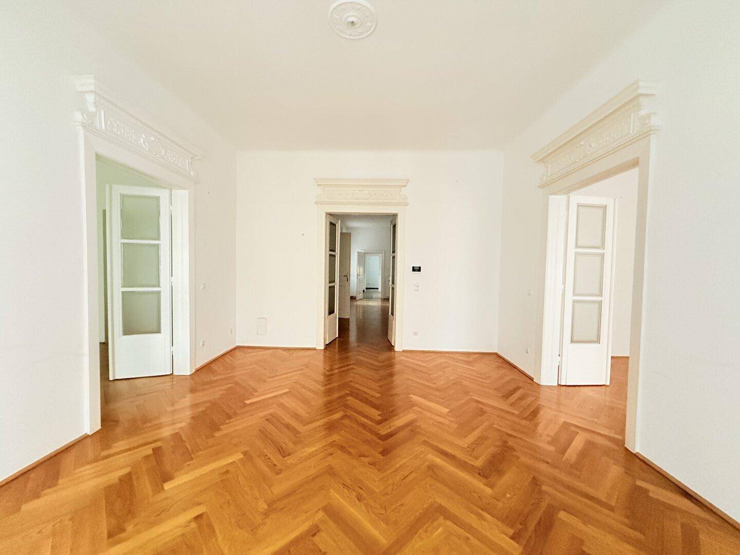 Großes Zimmer mit Fischgrätparkett und eleganten Türrahmen, ideal für Wohn- oder Schlafbereich.