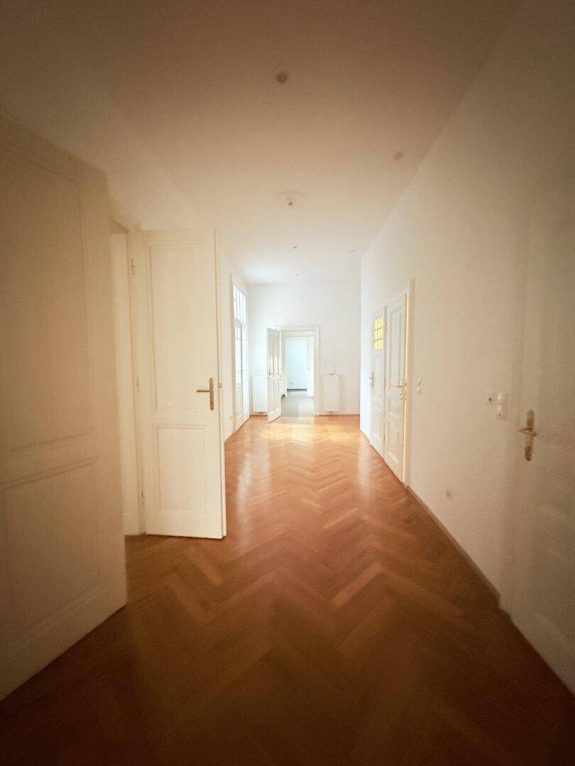 Langer Flur mit Fischgrätparkett und hohen Türen, der verschiedene Räume verbindet.