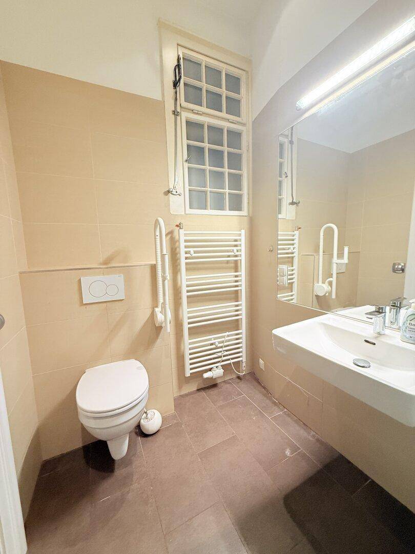 Helles Badezimmer mit Wand-WC, Waschbecken, beheiztem Handtuchhalter und Fenster.