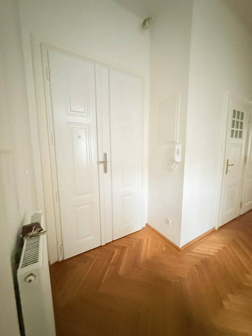 Eingangsbereich mit Fischgrätparkett, Heizkörper und hohen weißen Türen.