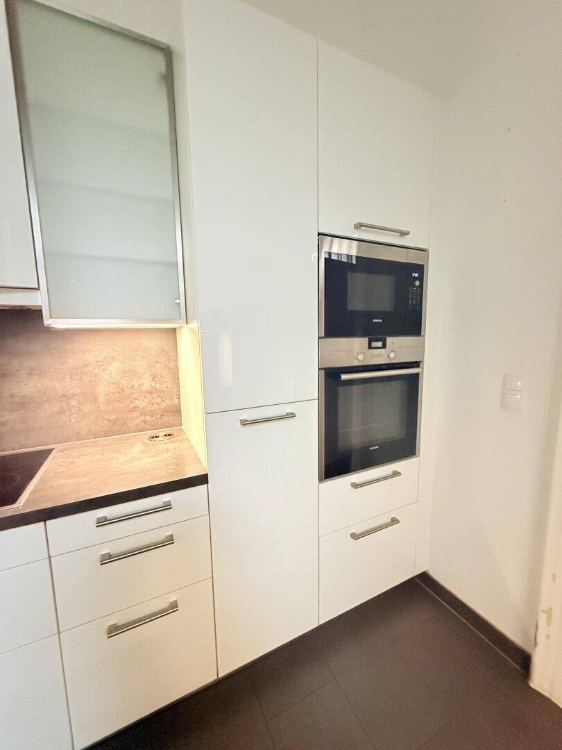 Moderne Einbauküche mit weißen Hochglanzschränken, integriertem Backofen und Mikrowelle.